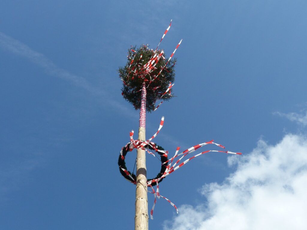Das Bild zeigt einen finnischen Mittsommerfestbaum. Dieser ist geschmückt mit grünen Kränzen und bunten Bändern.