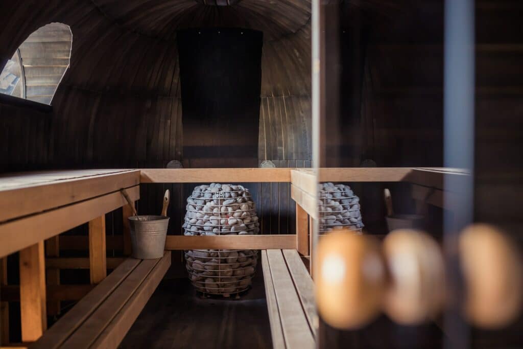 The picture shows a Finnish sauna from the inside. You can see wooden benches, a water bucket and sauna stones.